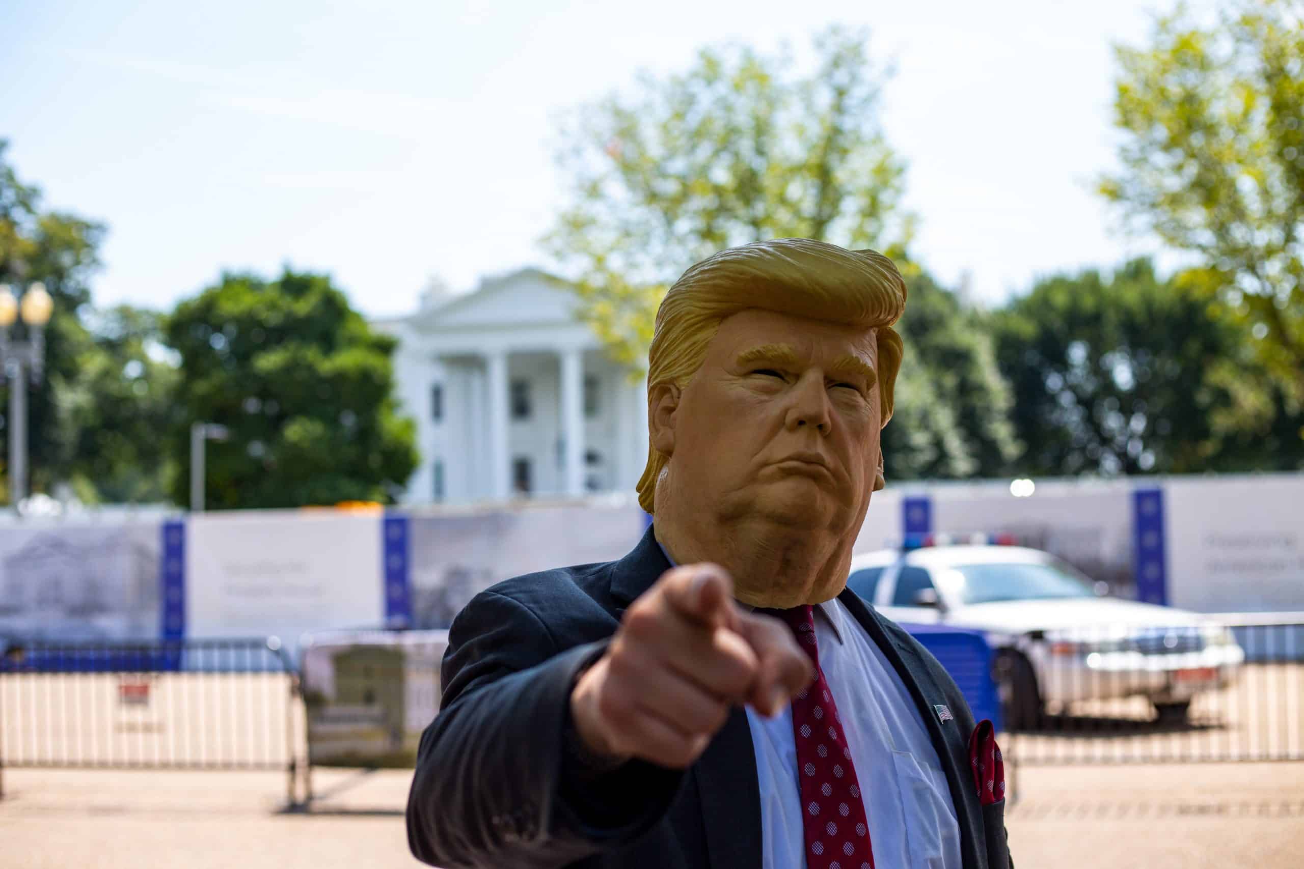 Une personne avec un masque Donald Trump devant la Maison Blanche