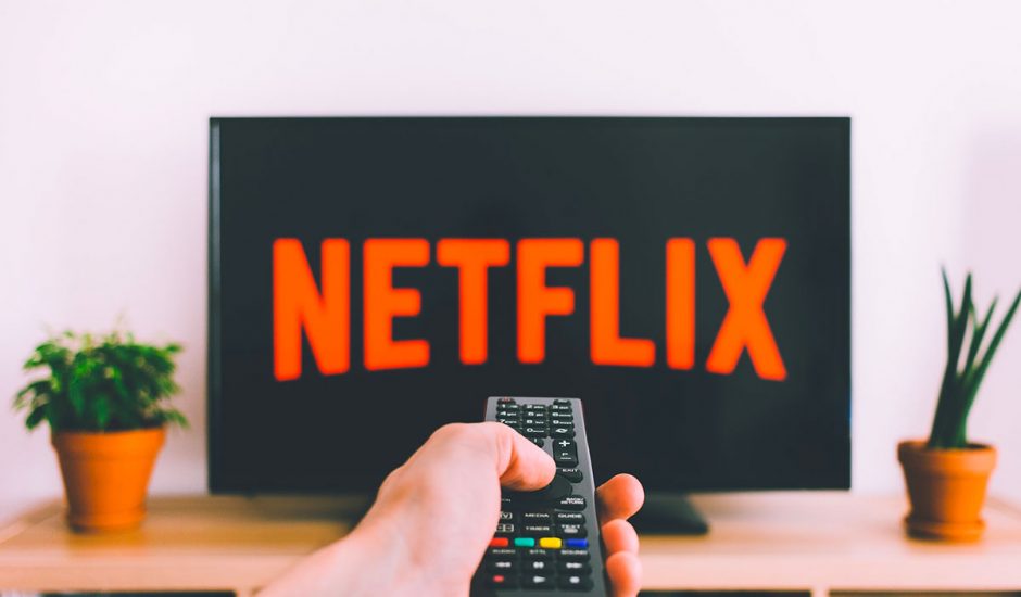 Netflix le logo sur une TV avec une personne qui tient sa télécommande