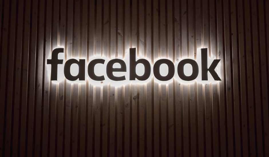 Le logo illuminé de Facebook sur un mur en bois.