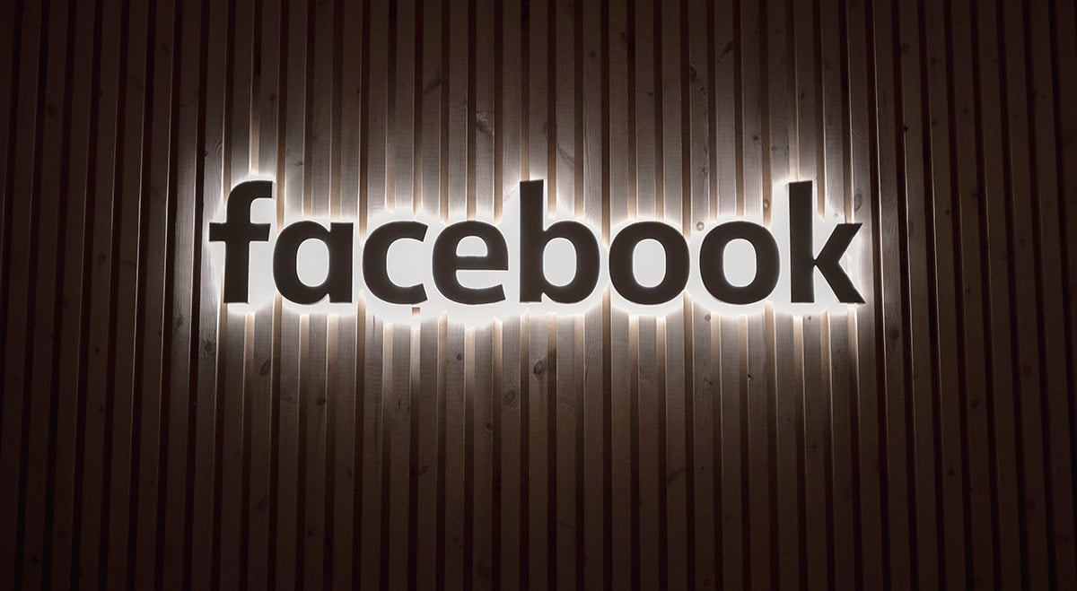 Le logo illuminé de Facebook sur un mur en bois.