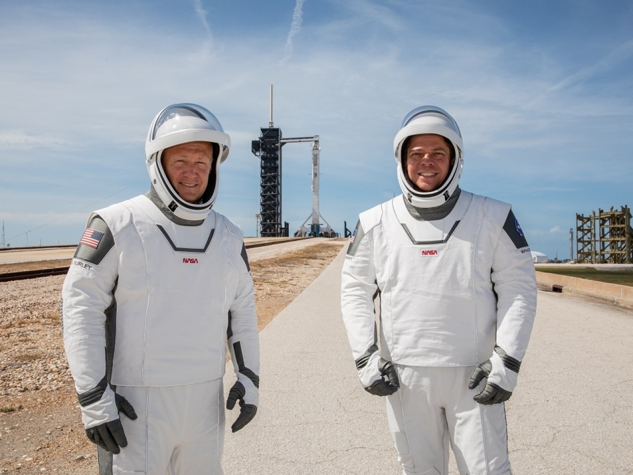 Les astronautes Doug Hurley et Bob Behnken se tiennent devant le site de lancement dans une combinaison spatiale signée SpaceX.