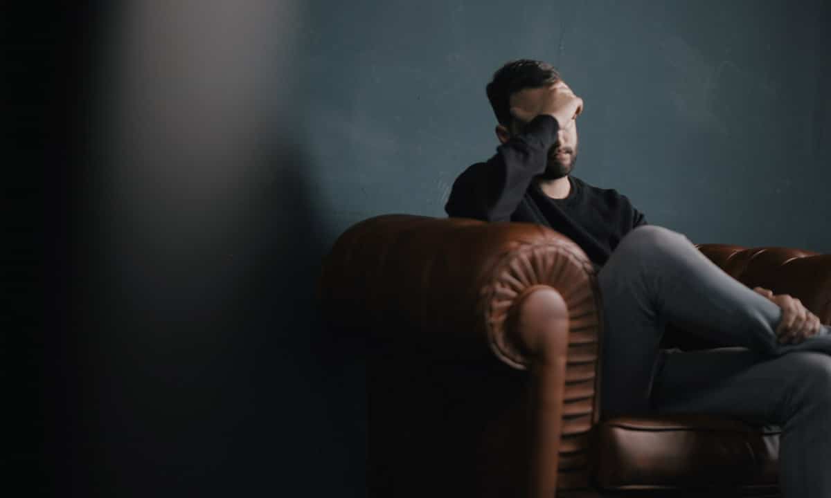 Un homme assis sur un fauteuil se tenant le visage.