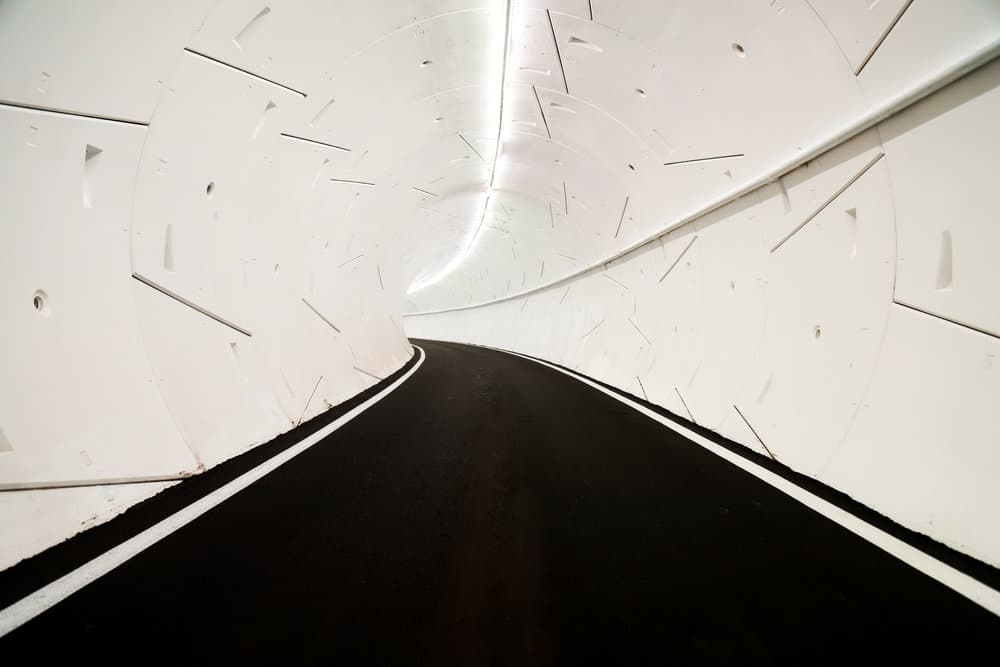 L'intérieur d'un tunnel de The Boring Company, avec une route entourée de parois blanches et futuristes.