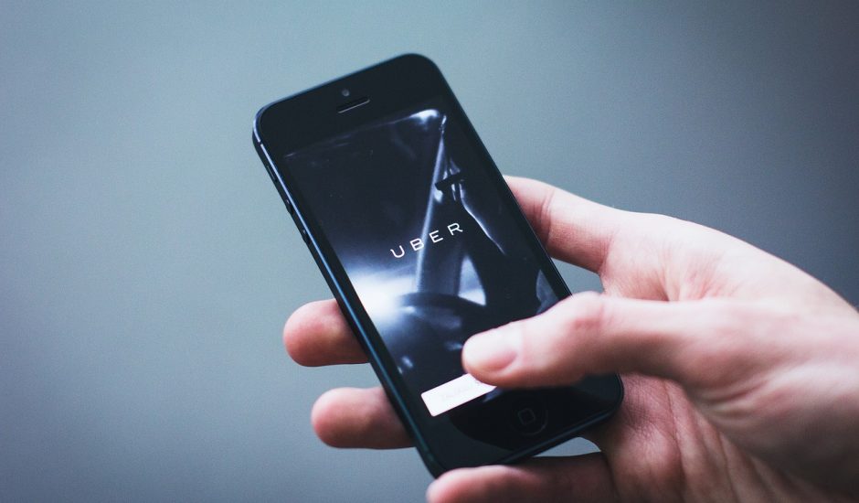 Une main tenant un smartphone ouvert sur l'application Uber.