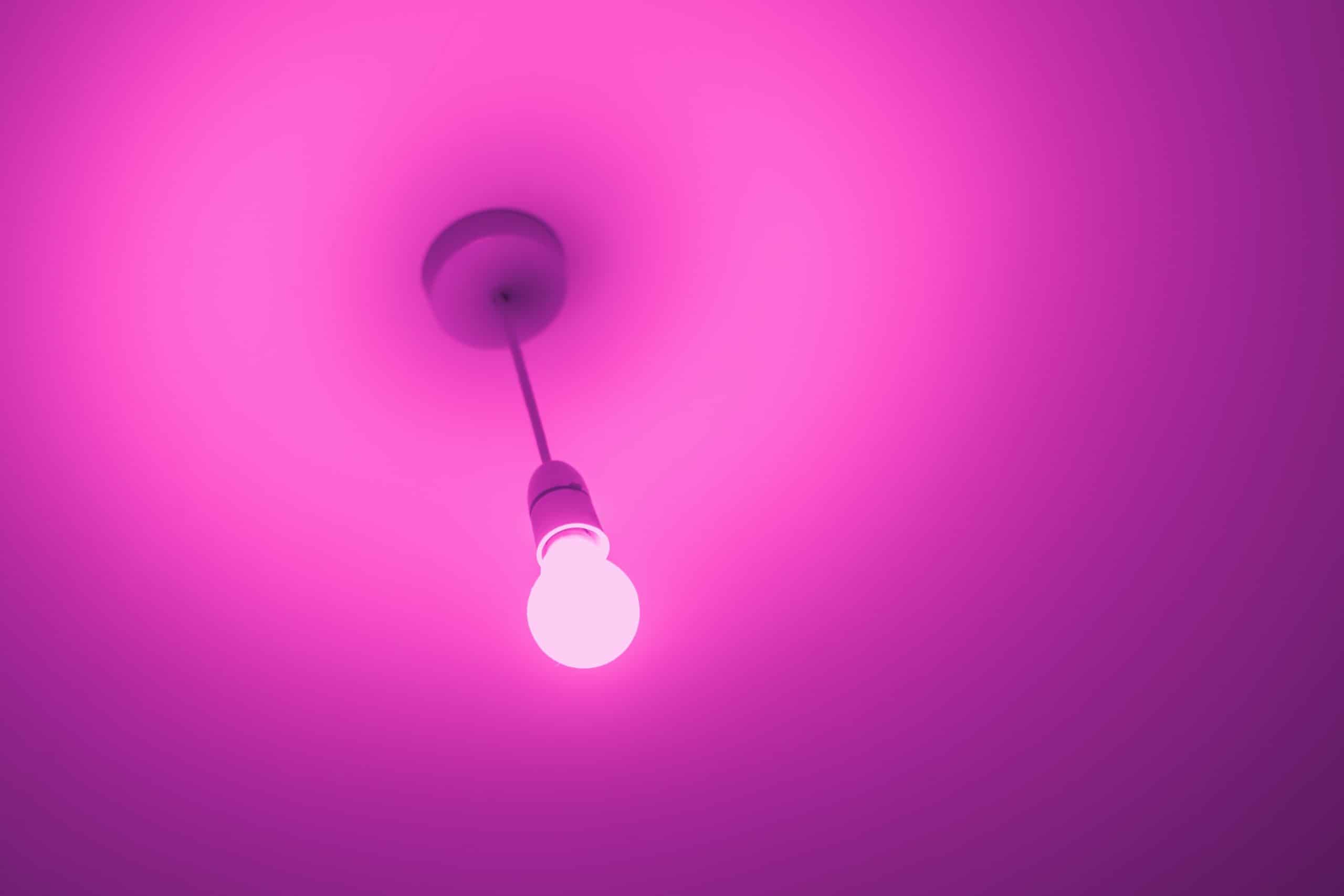 Une ampoule LED pend du plafond et émet de la lumière rose.