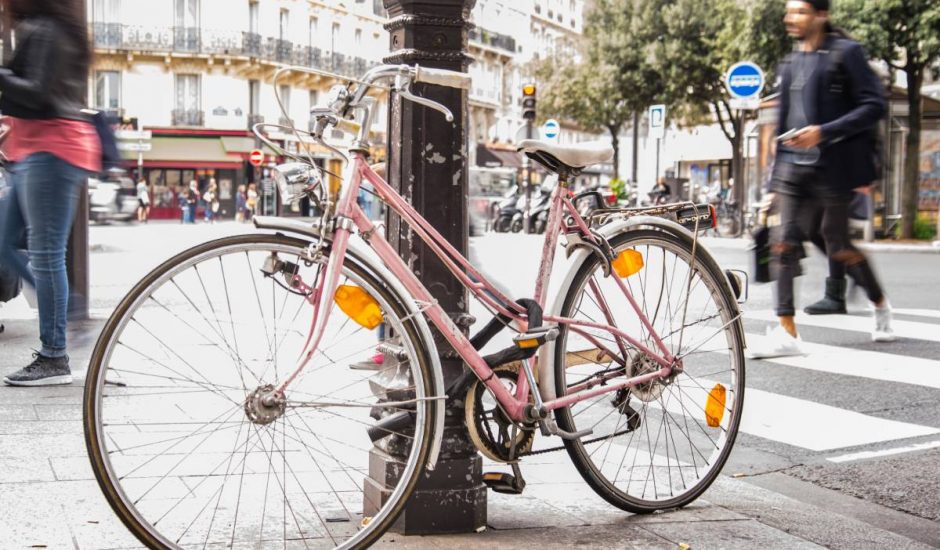 Un vélo rose accroché à un poteau dans les rues de Paris.