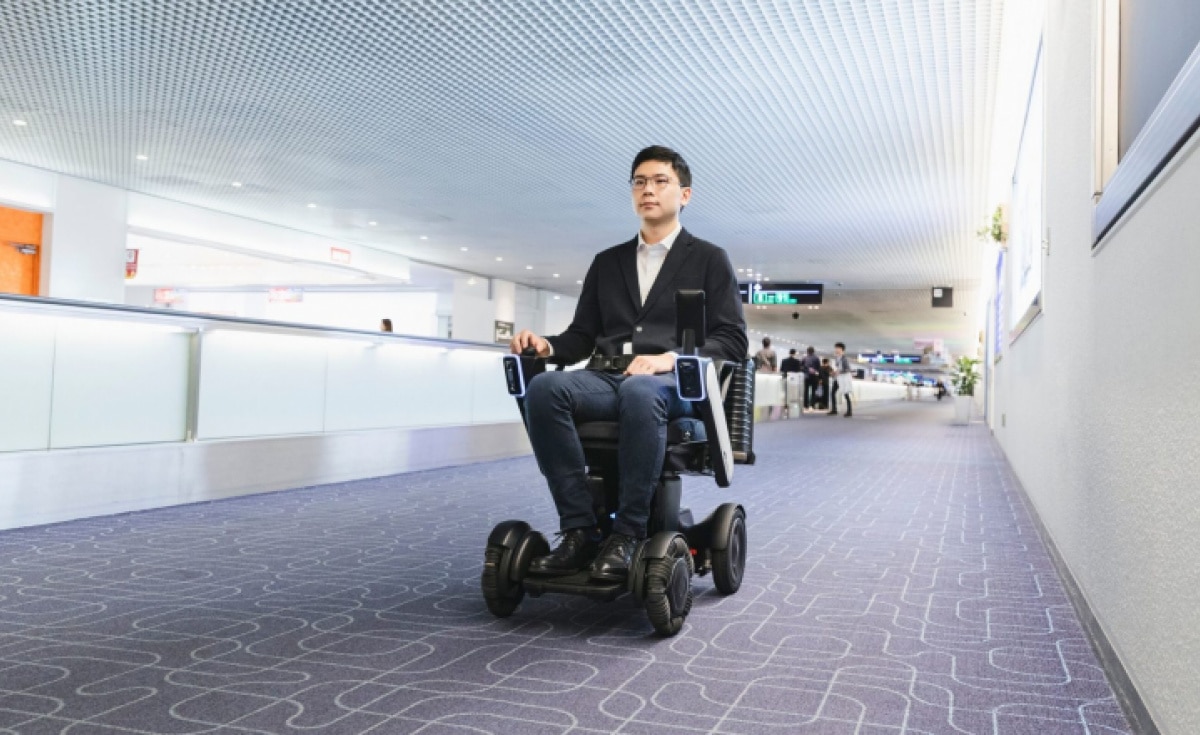 Un homme assis sur un fauteuil robotisé WHILL dans un aéroport.