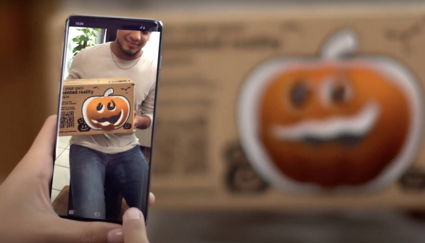 Un smartphone prend en photo l'image d'un emballage d'Amazon sur lequel se trouve un dessin de citrouille Jack O' Lantern.