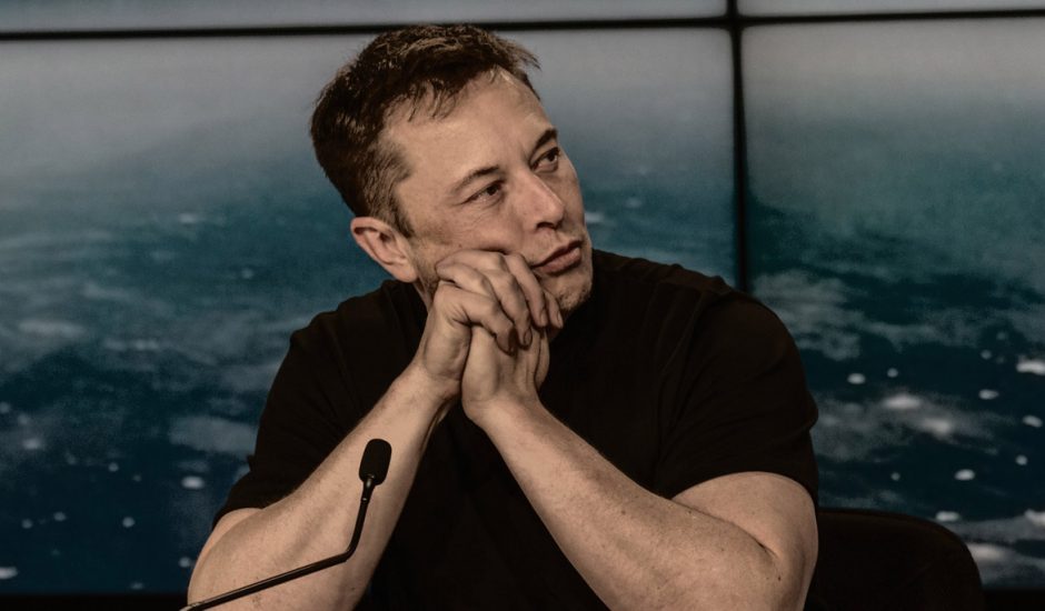 Elon Musk assis et accoudé à un bureau.