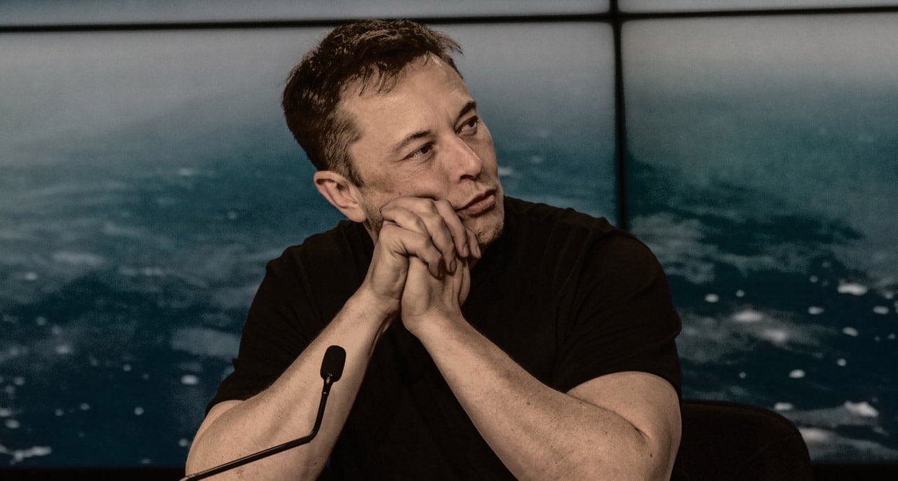 Elon Musk assis et accoudé à un bureau.