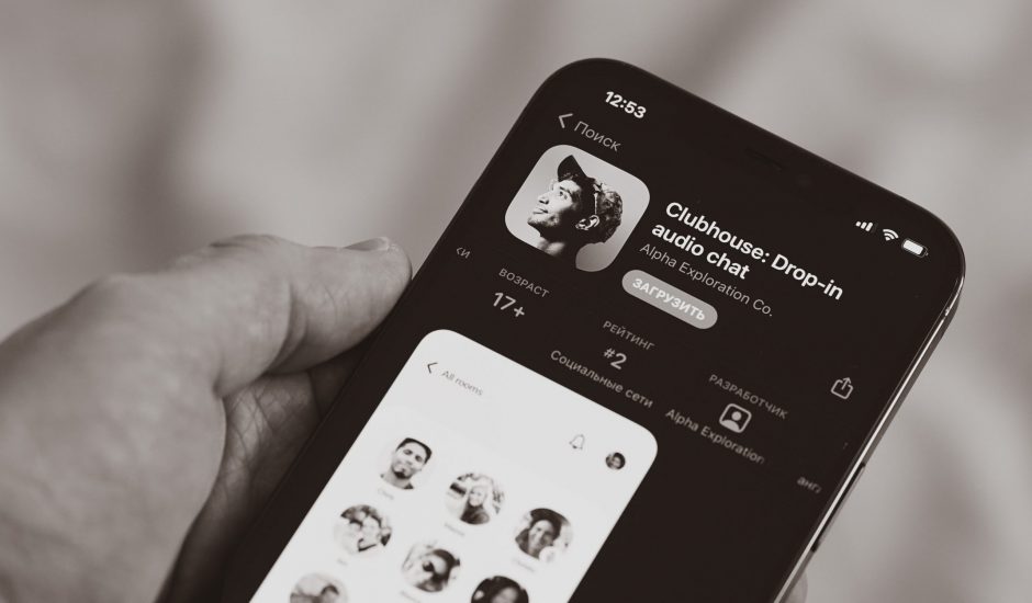 Une personne tenant un smartphone dans la main, avec la page de Clubhouse sur l'App Store d'Apple.