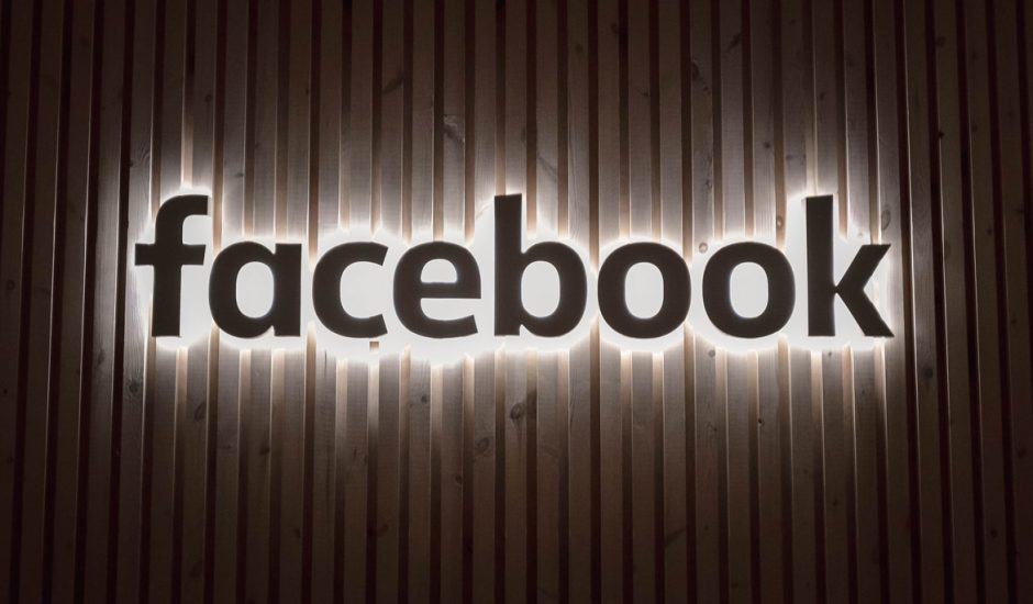 Le logo Facebook illuminé sur un mur en bois.