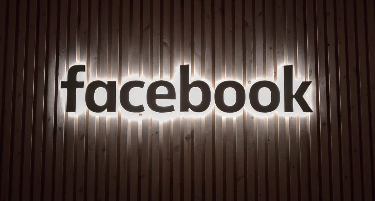 Le logo Facebook illuminé sur un mur en bois.
