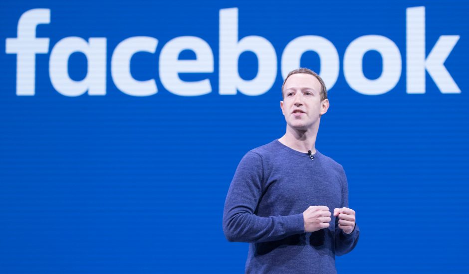 Mark Zuckerberg debout devant le logo de Facebook.