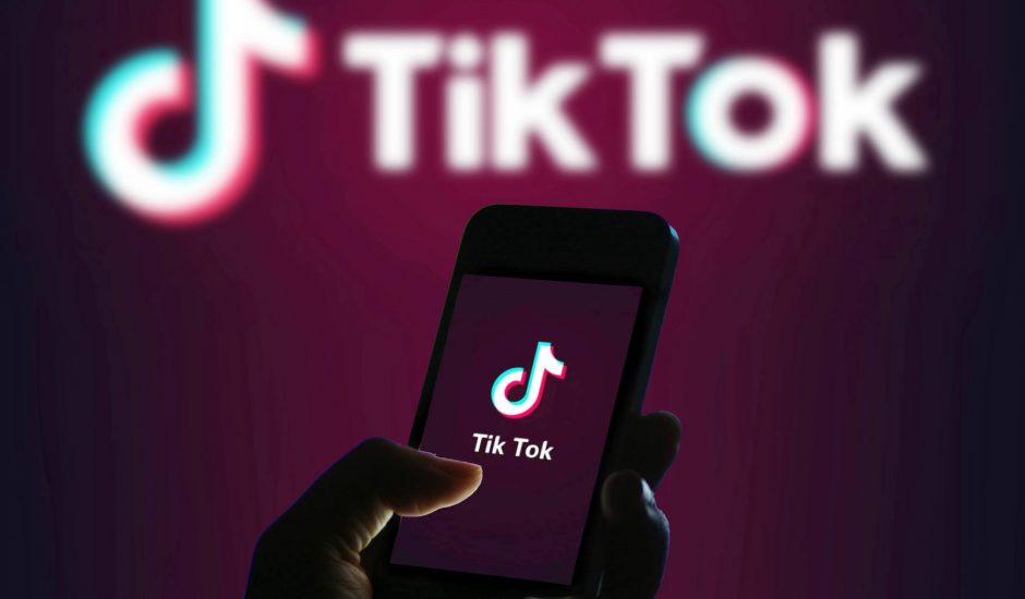 Photographie du logo TikTok avec une personne qui tient son portable dans les mains. La méthode de travail 996 est controversée.