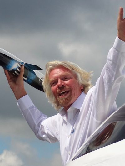 Portrait de Richard Branson tenant la maquette d'une fusée dans sa main.