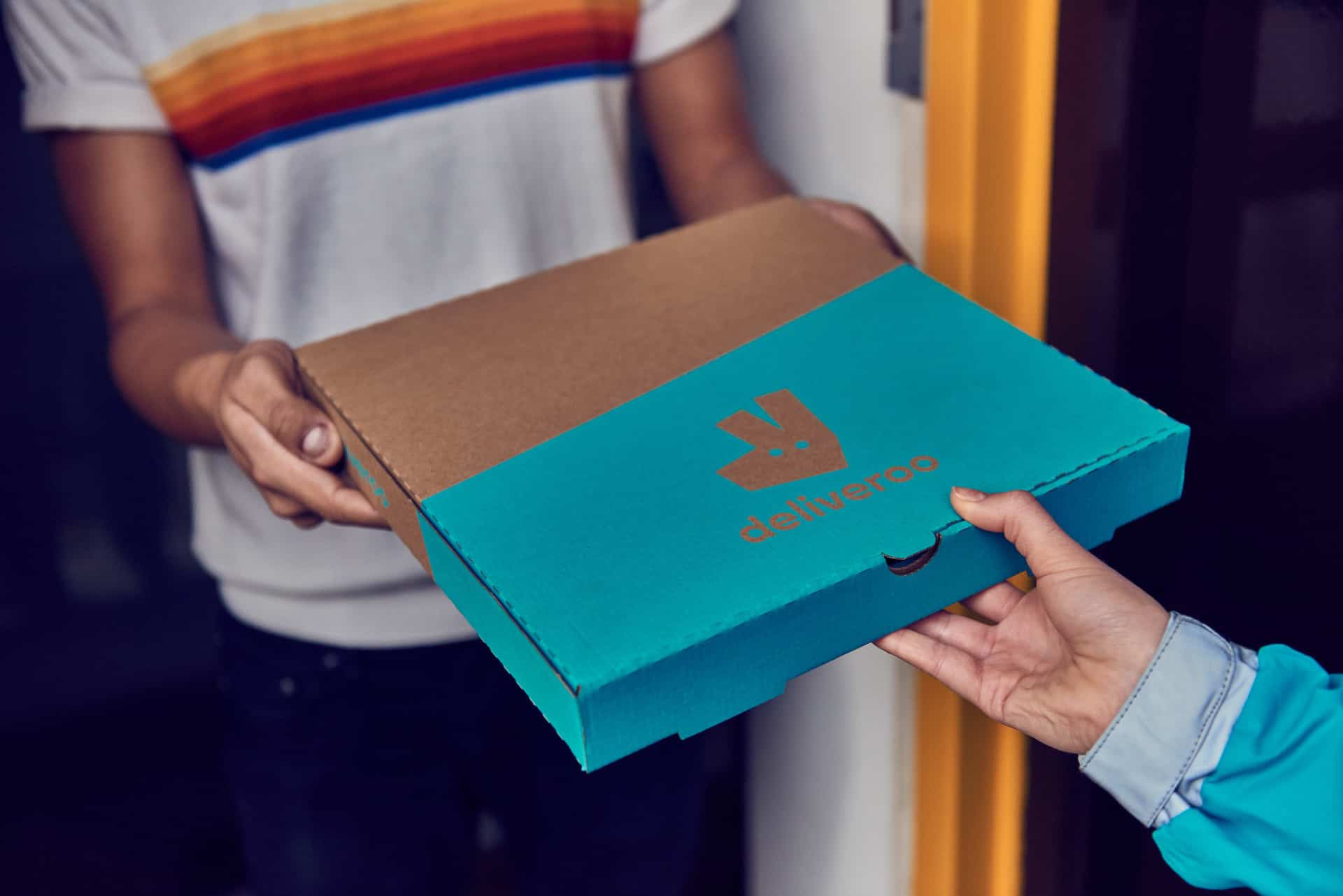 Une personne récupérant une pizza dans un carton Deliveroo.