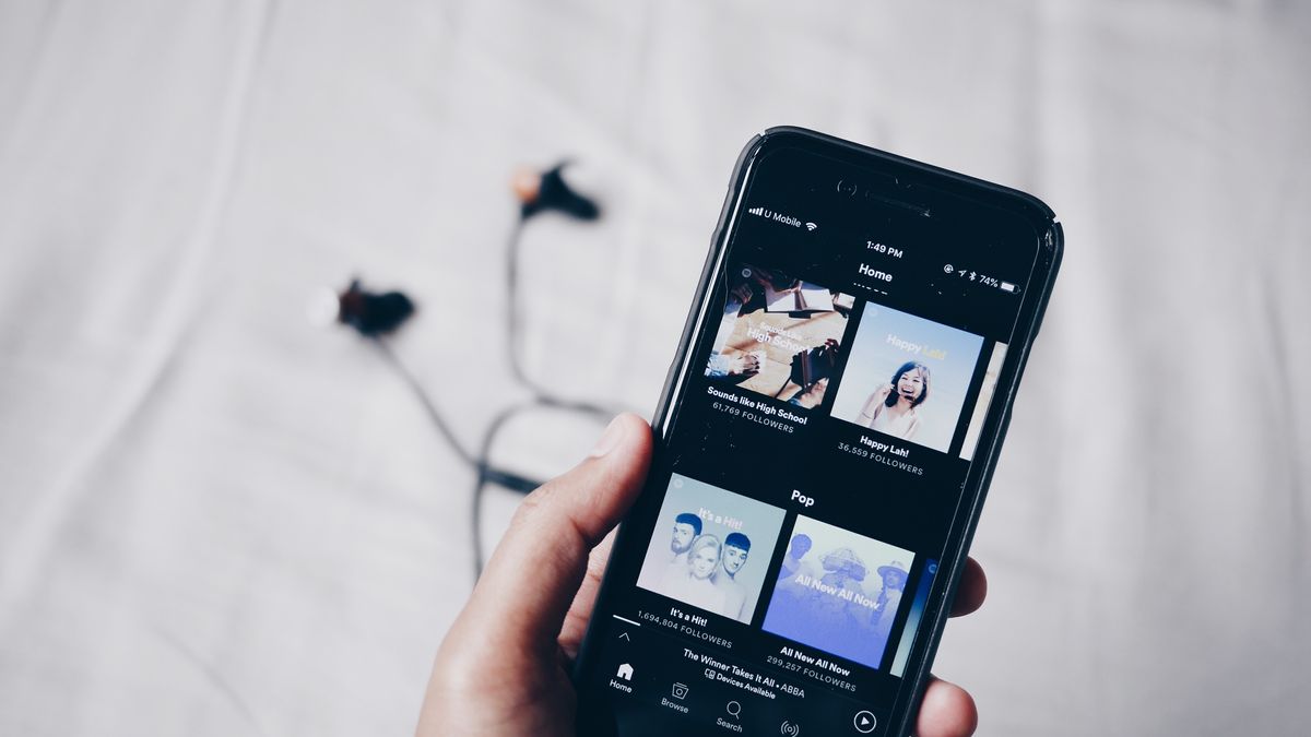 L'application Spotify sur un téléphone mobile avec des écouteurs en arrière plan.
