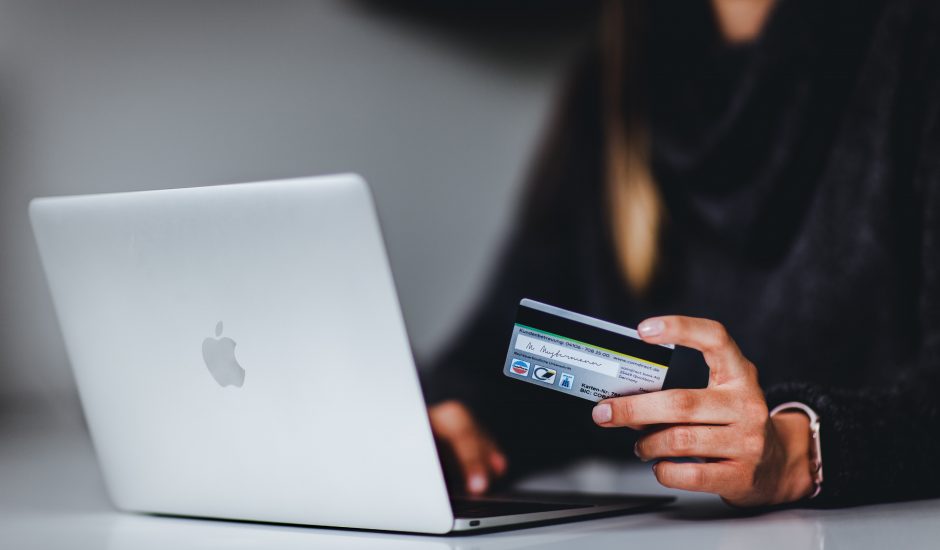 Une femme tient une carte de crédit dans la main alors qu'elle se tient sur son ordinateur.