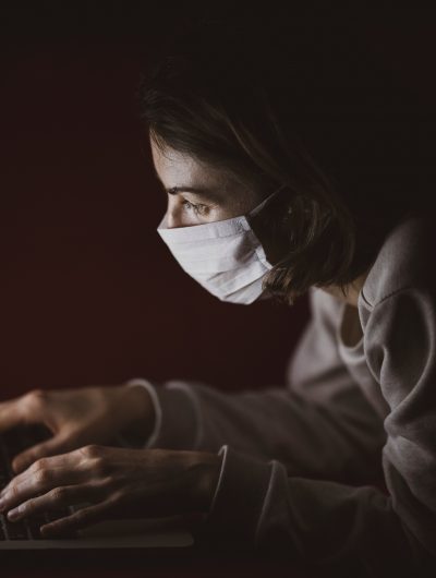 Une femme dans le noir portant une masque utilisant un ordinateur portable