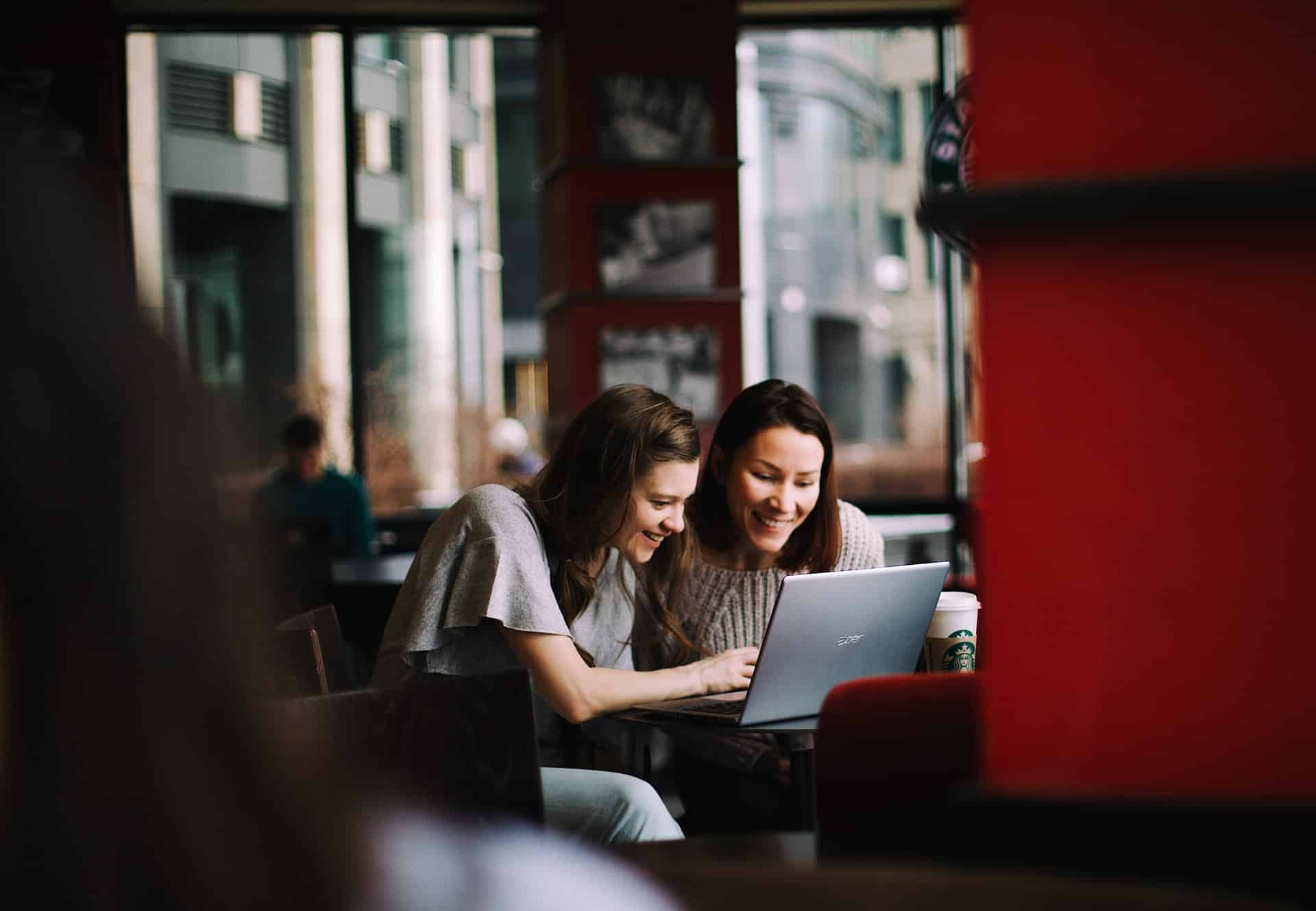 deux femmes souriant devant un ordinateur / marketing digital