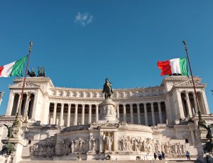 Deux drapeaux italiens flottent devant un monument.