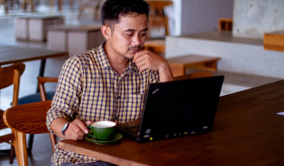 un homme devant un ordinateur avec une tasse verte posé à côté