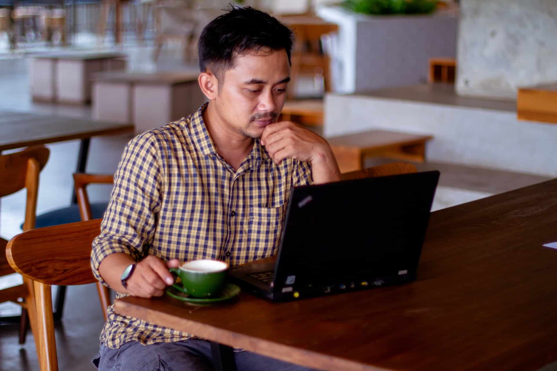 un homme devant un ordinateur avec une tasse verte posé à côté