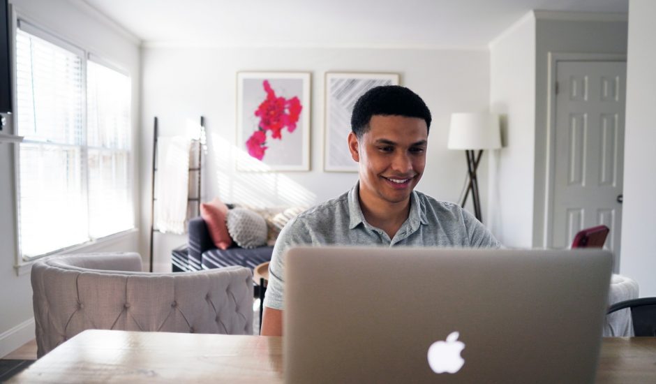 un homme souriant devant un ordinateur portable Apple