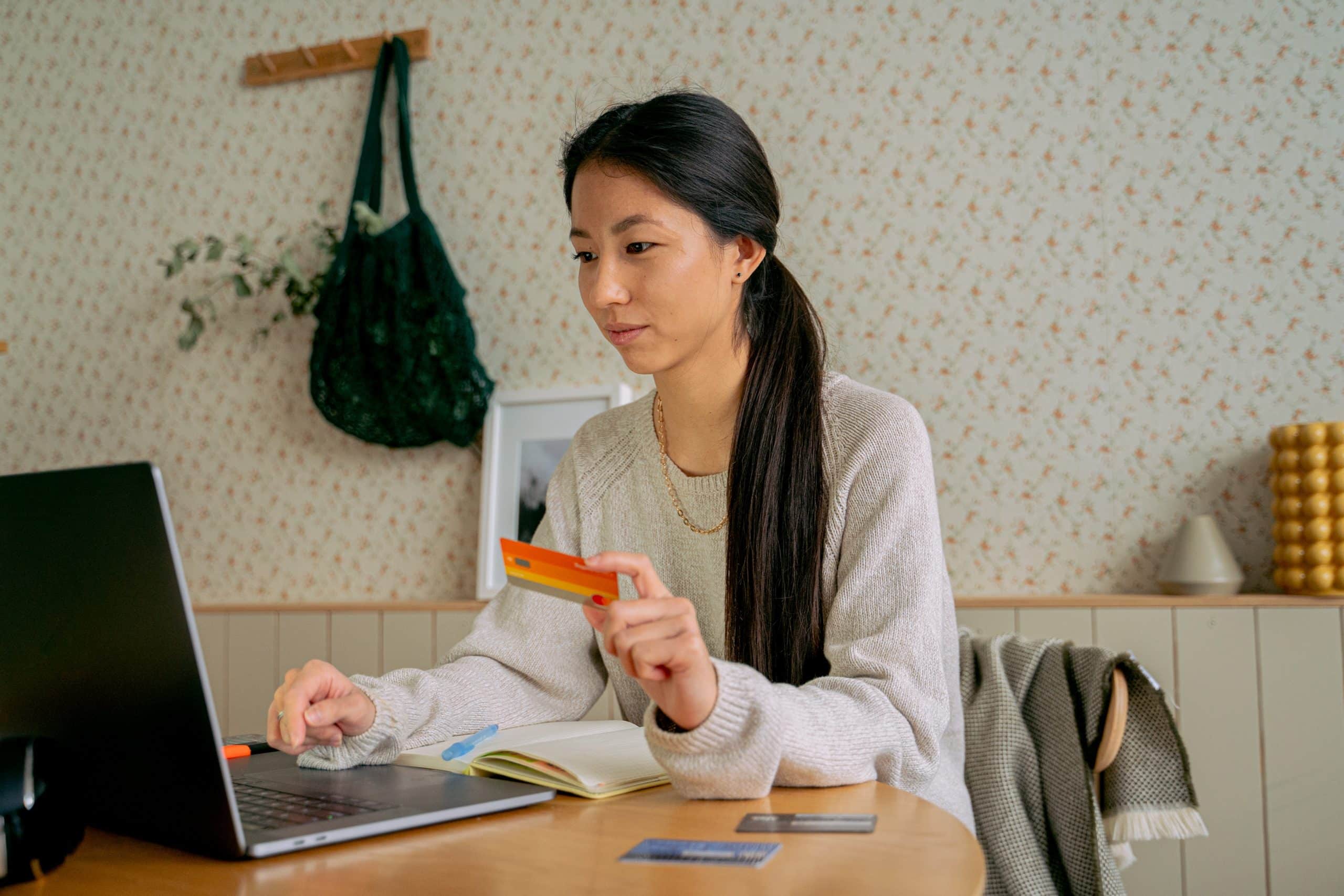 une femme tenant une carte bancaire orange dans la main, devant un ordinateur