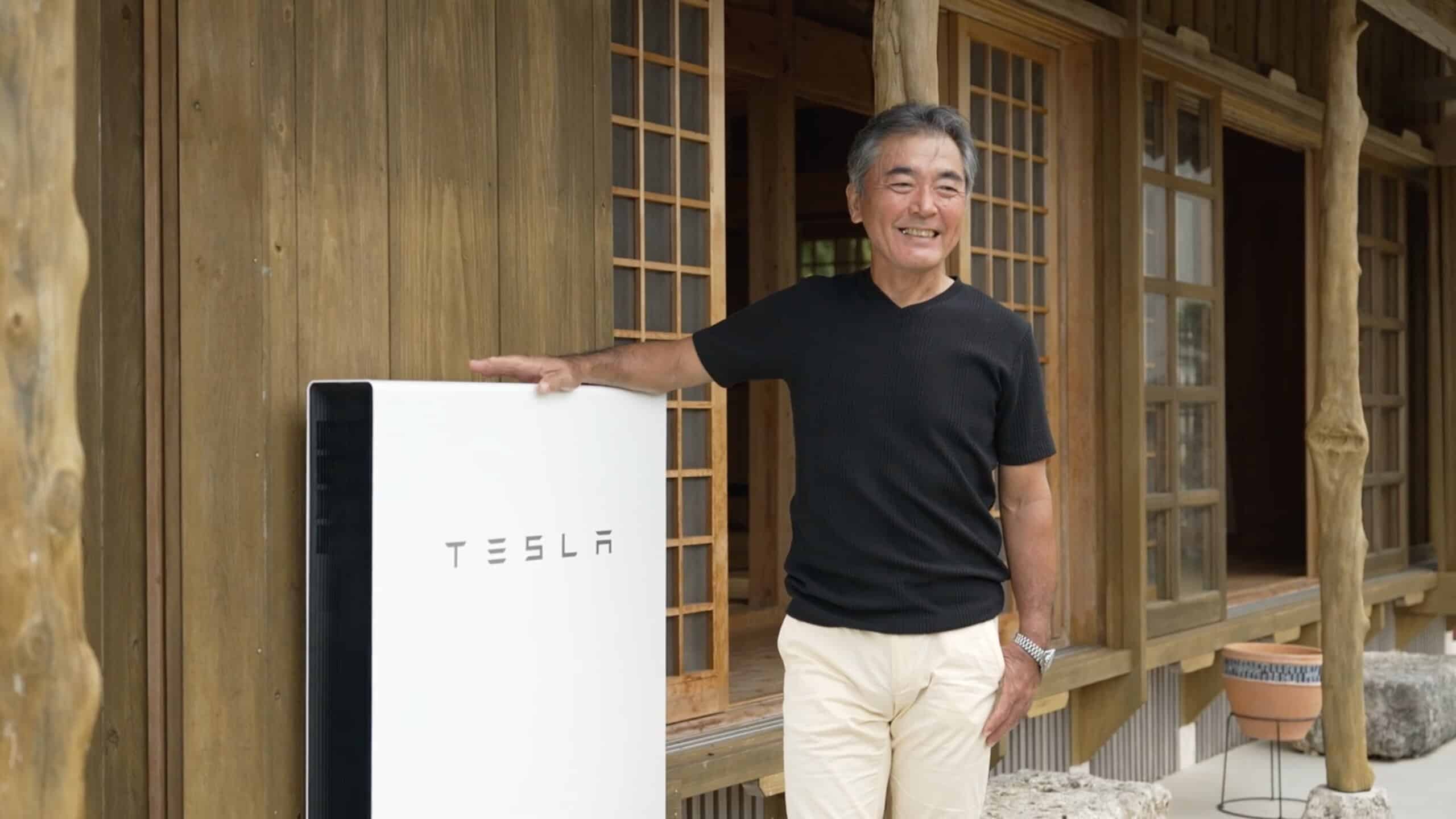 Un homme japonais devant sa maison posant à côté d'une batterie Tesla