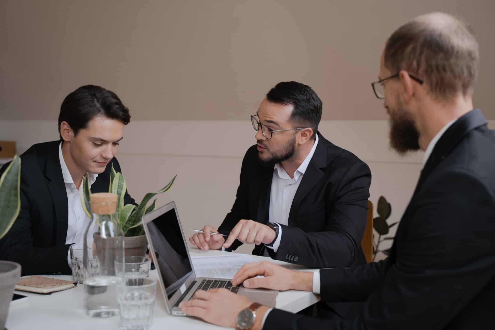 trois hommes en costume devant une table avec un ordinateur portable et des papiers