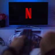 Photographie d'une télé affichant le logo Netflix et qui est regardé par une personne