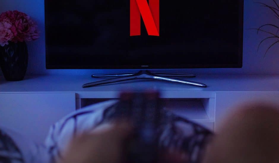 Photographie d'une télé affichant le logo Netflix et qui est regardé par une personne