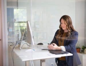 une femme debout devant un ordinateur, elle regarde son téléphone