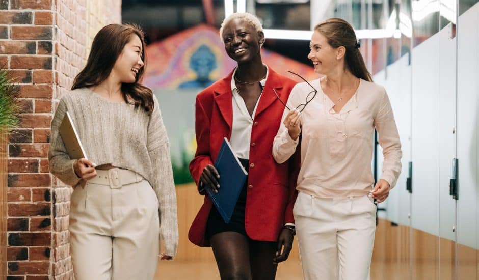 trois femmes souriantes marchant dans les couloirs d'une entreprise