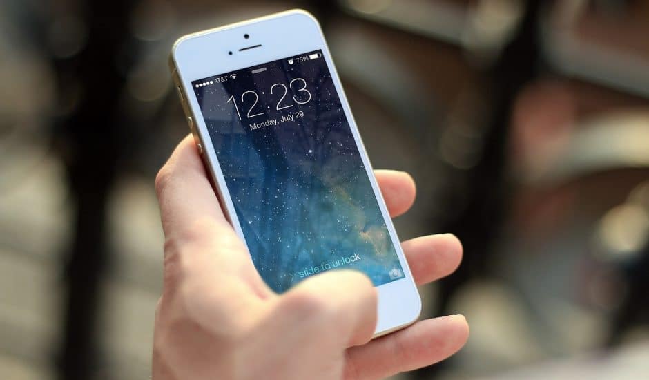 Une main tenant un Iphone blanc à l'écran allumé.