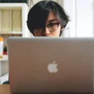 une homme avec des lunettes derrière un macbook