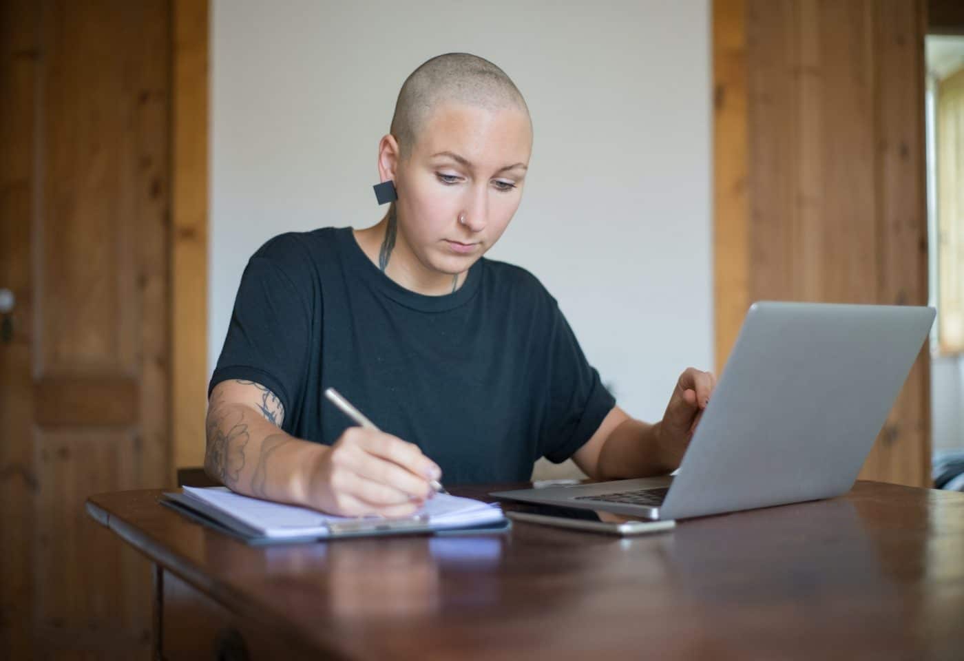 une femme en train d'écrire sur un papier avec sa main droite, sur son ordinateur avec la main gauche