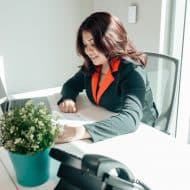 une femme à un bureau sur son ordinateur, une petite plante et un téléphone devant elle