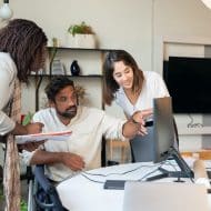 deux femmes et un homme devant un bureau, fixant un ordinateur