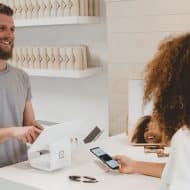 une femme en train de payer avec son mobile dans un magasin, un homme caissier en face
