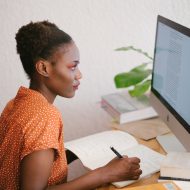une femme devant son ordinateur en train de prendre des notes