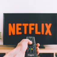 Une main tenant une télécommande pointée vers une télévision avec le logo de Netflix affiché