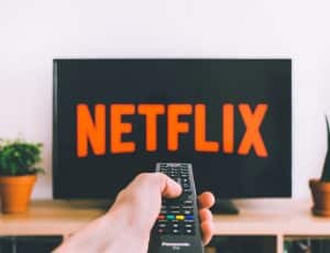 Une main tenant une télécommande pointée vers une télévision avec le logo de Netflix affiché