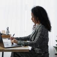 une femme sur son ordinateur qui prend des notes sur un carnet à côté d'elle. Vue de côté
