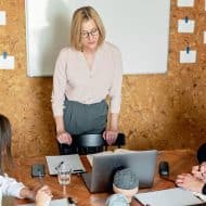 une équipe en réunion : deux personnes assises, une femme debout devant un ordinateur. Des papiers accrochés au mur