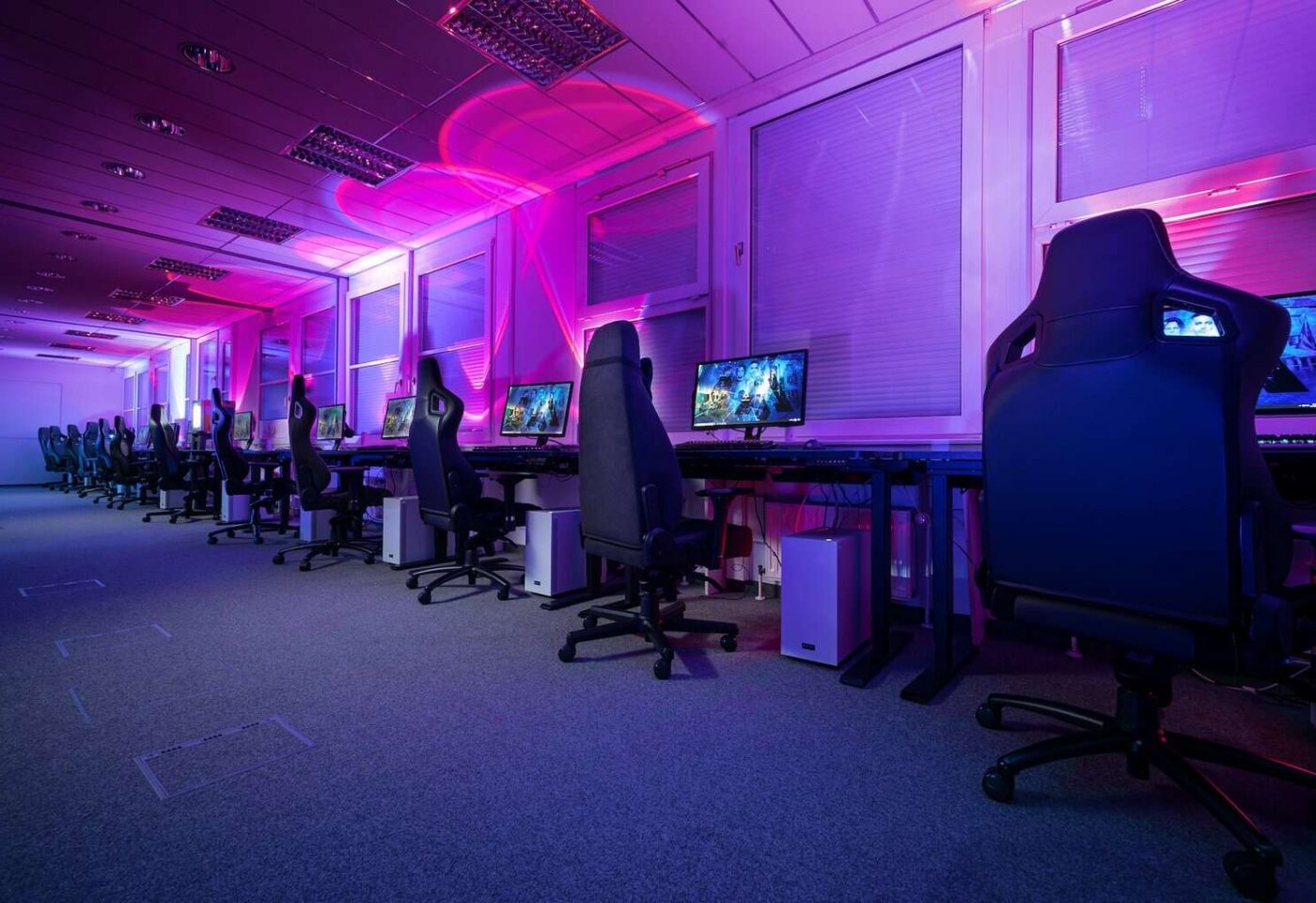 Salle avec plusieurs chaises de games en ligne et une multitude de postes d'ordinateur pour jouer à des jeux vidéo.