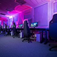 Salle avec plusieurs chaises de games en ligne et une multitude de postes d'ordinateur pour jouer à des jeux vidéo.
