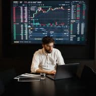 un homme sur un ordinateur avec les statistiques de la bourse derrière lui